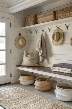 a white bench with baskets and hats hanging on the wall next to an open door