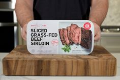 a man holding a box of sliced grass - fed beef sirloin on a cutting board