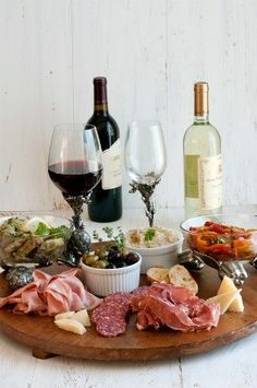 a table topped with wine glasses filled with different types of food and meats next to bottles of wine