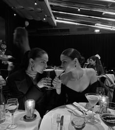 two women sitting at a table with wine glasses in front of their faces and one holding a glass up to her mouth