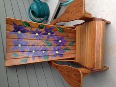 a wooden chair with flowers painted on it's back and seat, next to a watering can