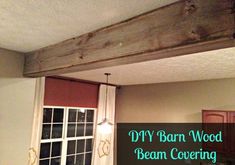 a wooden beam hanging from the ceiling above a kitchen sink and counter top with text overlay that reads diy barn wood beam covering