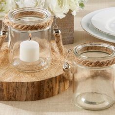 there is a glass jar with a candle in it on a wooden stand next to plates and flowers