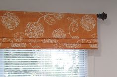 a window with an orange and white flowered valance