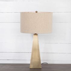 a table lamp with a beige shade on it and a white wall in the background