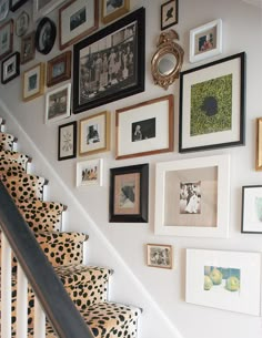 there are many framed pictures on the wall next to the stair case and handrail