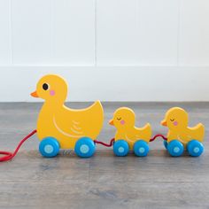 a wooden toy ducky and two rubber ducks pulling a red string on a wood floor