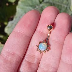 a person is holding a gold nose ring with an opalite in the middle