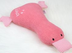 a pink whale stuffed animal laying on top of a white fur covered floor with its mouth open