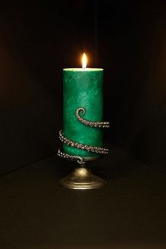 a green candle sitting on top of a metal stand with a chain wrapped around it