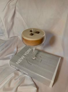 a drink sitting on top of a new york cookbook with two olives in it