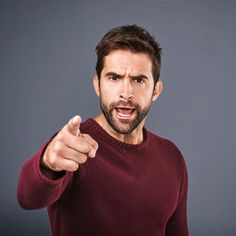 a man pointing to the side with his hand on his hip and wearing a red sweater