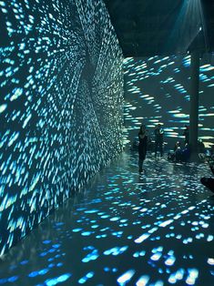 people are standing in front of a large wall with many lights on it and the floor is covered in water droplets