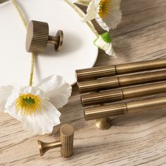 some white flowers and brass knobs on a wooden table next to a plate with gold handles