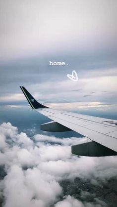 an airplane wing flying above the clouds with some writing on it's side that says home