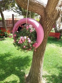 a pink tire hanging from a tree with flowers in the center and on it's side