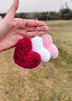 three crocheted heart keychains are being held by a person's hand