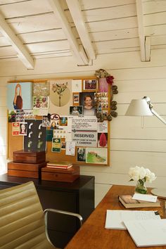 a room with a desk, chair and bulletin board on the wall above it is covered in pictures