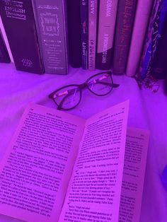 an open book sitting on top of a bed next to some purple glasses and books