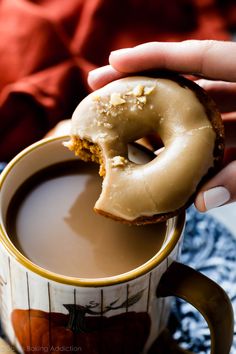 a person holding a donut in their hand over a cup of hot chocolate coffee