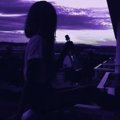 a woman is sitting on a ledge with her back to the camera and looking at the sky