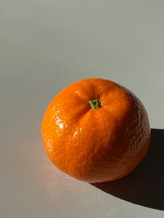 an orange sitting on top of a white table next to a shadow from the sun