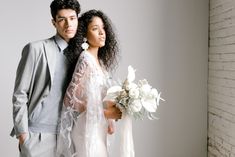 a man and woman standing next to each other in front of a white brick wall