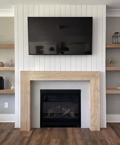 a television mounted on the wall above a fireplace in a room with wood floors and white walls