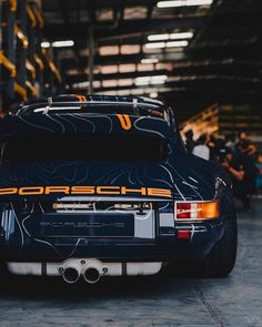 the back end of a black porsche parked in a garage with people looking at it