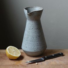 a stone vase sitting on top of a wooden table next to a knife and lemon