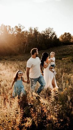 a family walking through tall grass with the sun shining down on them and trees in the background