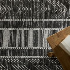 a black and white patterned rug with wooden cutting board on the floor next to it