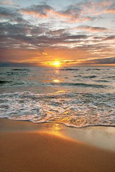 the sun is setting over the ocean with waves coming in to shore and sand on the beach