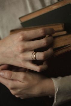 a woman holding a book with her hands on top of it and wearing a wedding ring