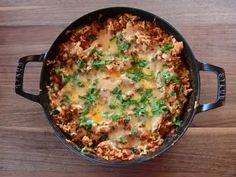 a casserole with meat, cheese and parsley in a black pan on a wooden table