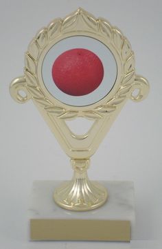 a gold trophy with a red apple in the center on a marble base for display