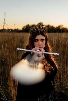 a woman blowing bubbles in the middle of a field with trees and grass behind her