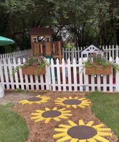 a garden with sunflowers painted on the ground in front of a white picket fence