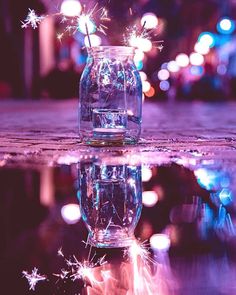 a glass jar filled with water and sparklers on top of a table next to a puddle