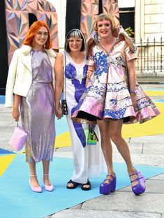 three women standing next to each other on a blue carpet