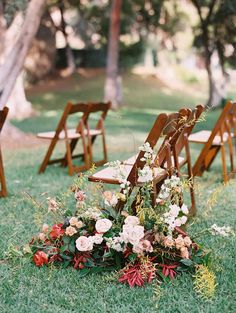 an arrangement of flowers and wooden chairs on the grass at a wedding ceremony in front of trees