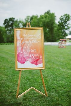 an easel with a wedding sign on it sitting in the middle of a field