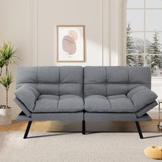 a living room with a gray couch and potted plant on the floor next to it