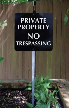 a private property no trespassing sign in front of a wooden fence with plants