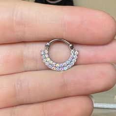 someone is holding their finger in front of the camera and wearing an open ring with multicolored stones on it