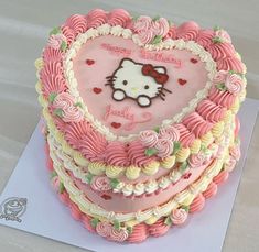 a heart shaped cake with pink frosting and hello kitty on it's side