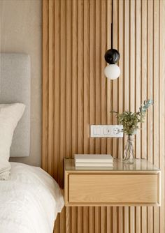 a nightstand with two books on it next to a white bed and wooden slatted walls