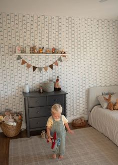 a little boy standing in the middle of a room next to a dresser and bed