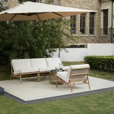 two chairs and an umbrella on a rug in front of a building with trees, grass and bushes