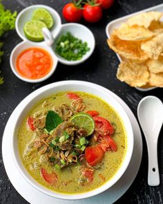 a bowl of soup with tortilla chips, tomatoes and limes on the side